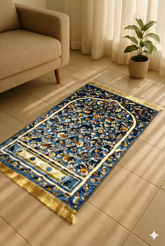 Blue Islamic prayer mat with floral patterns and gold fringes on beige tiled floor near beige sofa and green potted plant