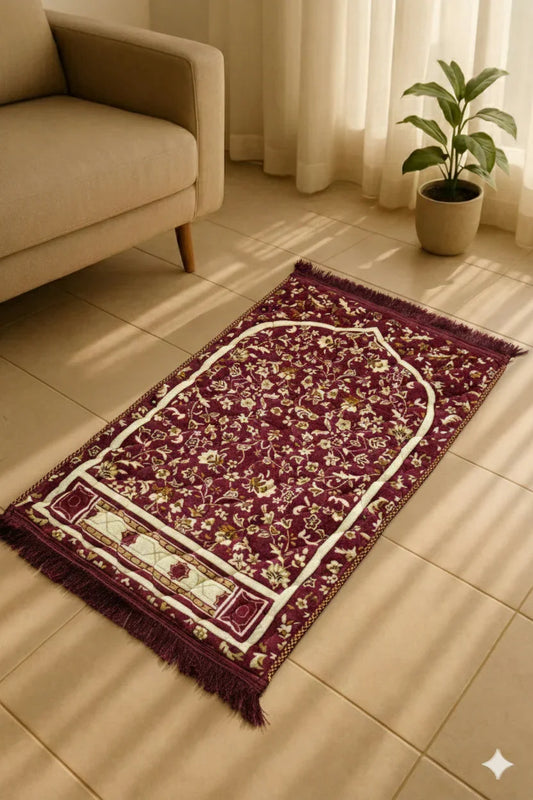 Maroon Islamic prayer mat with floral design placed on tiled floor near beige sofa and potted plant