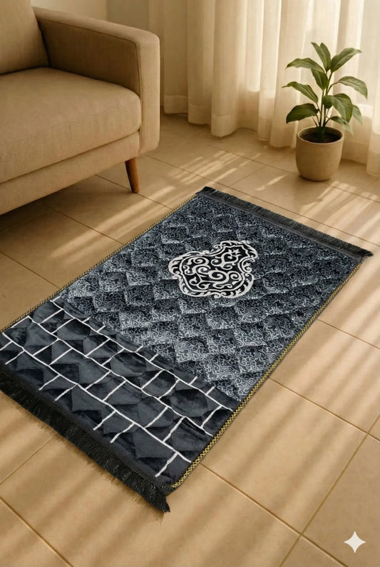 Elegant black and white Islamic prayer mat with geometric and floral patterns on tiled floor near beige sofa and potted plant